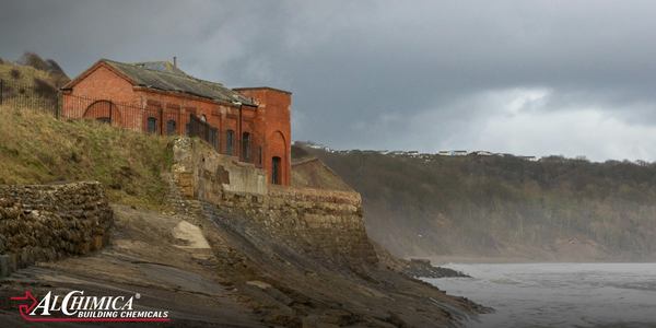 Coastal building on eroding shoreline with exposed foundations and stormy sea conditions, illustrating the impact of coastal erosion on structures